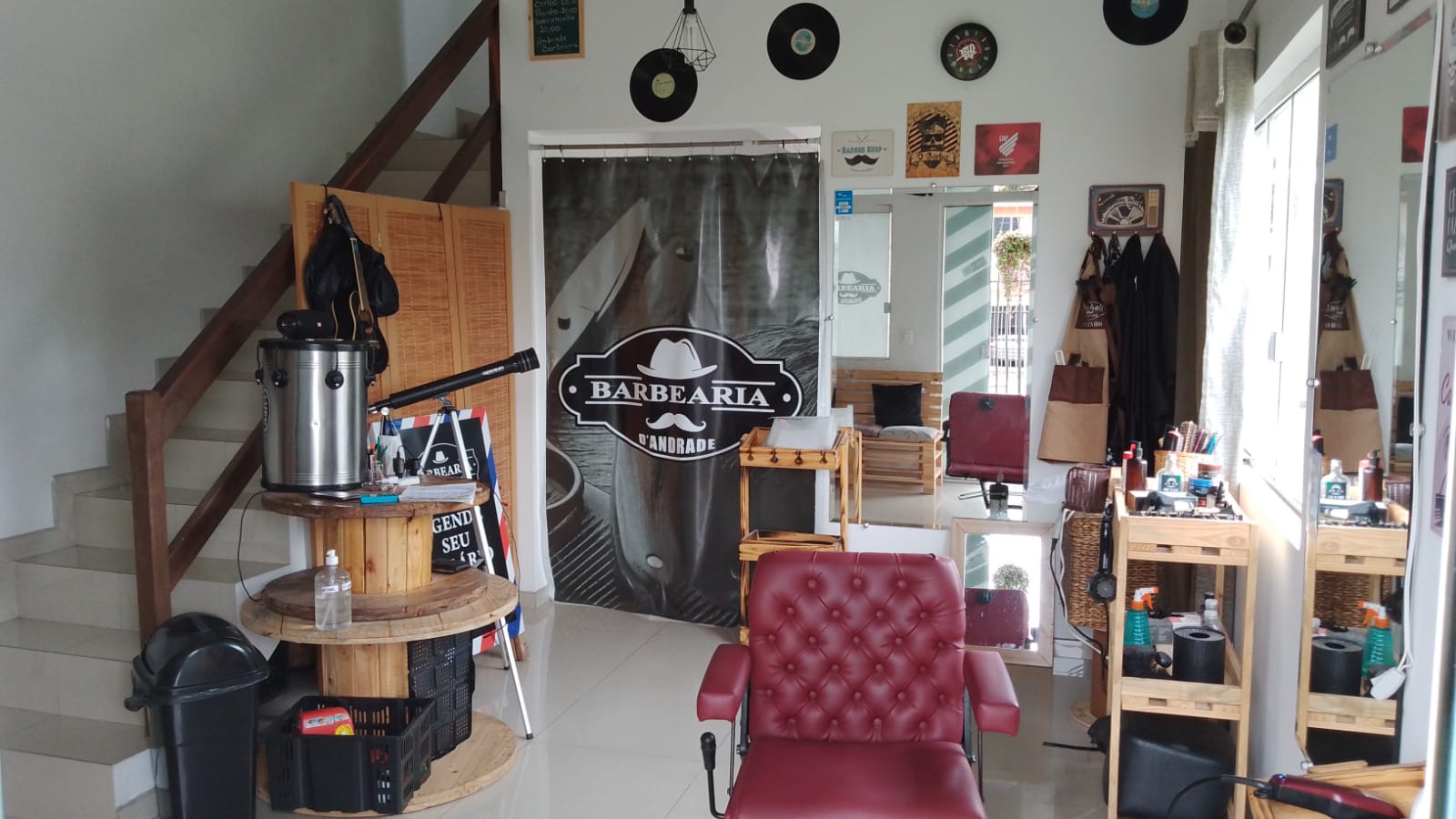 Interior da Barbearia D'Andrade, com cadeira de barbeiro vermelha e cortina com a logo do negócio
