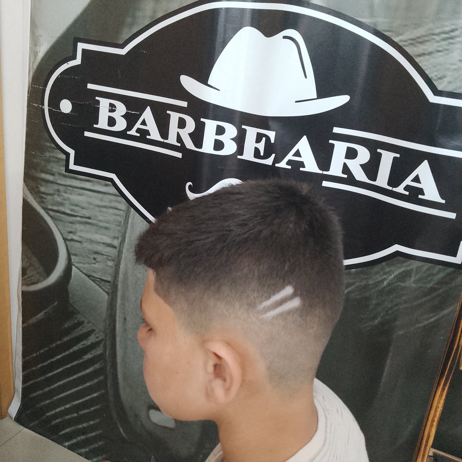 Detalhe de um desenho raspado na nuca, com a letra K, feito na Barbearia D'Andrade